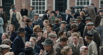 Movie still from “The Last Vermeer” (2019), directed by Dan Friedkin – A group of people in hats and suits gathered together; Wide shot, High angle