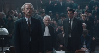 Movie still from “The Last Vermeer” (2019), directed by Dan Friedkin – A group of men in suits standing in front of a crowd of onlookers; Medium shot, Low angle