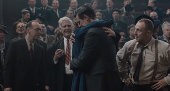 Movie still from “The Last Vermeer” (2019), directed by Dan Friedkin – A man hugging a woman in front of an audience; Medium shot, Over the shoulder angle