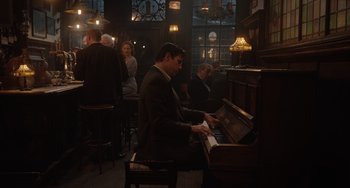 Movie still from “The Last Vermeer” (2019), directed by Dan Friedkin – A man sitting in front of an upright piano in a bar; Wide shot, Low angle