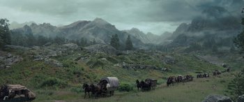 Movie still from “The Last Voyage of the Demeter” (2023), directed by André Øvredal – A group of horses pulling a wagon down a dirt road; Extreme Wide shot, High angle