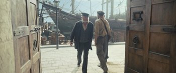 Movie still from “The Last Voyage of the Demeter” (2023), directed by André Øvredal – Two men walking down the street in front of some ships; Wide shot, Over the shoulder angle