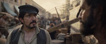 Movie still from “The Last Voyage of the Demeter” (2023), directed by André Øvredal – A man with a beard wearing a black hat; Close Up shot, Over the shoulder angle
