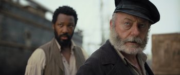 Movie still from “The Last Voyage of the Demeter” (2023), directed by André Øvredal – Two men standing next to each other on a sunny day; Close Up shot, Low angle