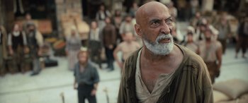 Movie still from “The Last Voyage of the Demeter” (2023), directed by André Øvredal – An old man with a beard is standing in front of a group of people; Medium shot, Over the shoulder angle