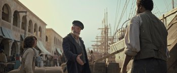 Movie still from “The Last Voyage of the Demeter” (2023), directed by André Øvredal – An old man in a hat and a coat is standing in front of a ship; Medium shot, Low angle