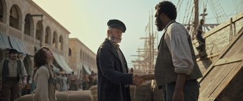 Movie still from “The Last Voyage of the Demeter” (2023), directed by André Øvredal – Two men shaking hands in front of some ships; Medium shot, Over the shoulder angle
