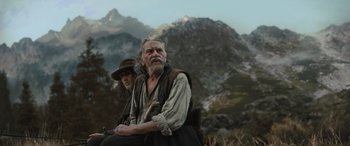 Movie still from “The Last Voyage of the Demeter” (2023), directed by André Øvredal – A man and a woman sitting on a bench in a field; Medium shot, Low angle