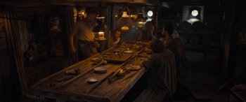 Movie still from “The Last Voyage of the Demeter” (2023), directed by André Øvredal – A group of people sitting around a wooden table; Wide shot, High angle
