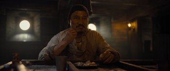Movie still from “The Last Voyage of the Demeter” (2023), directed by André Øvredal – A man sitting at a table with a plate of food in front of him; Close Up shot, Low angle