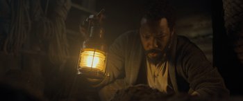 Movie still from “The Last Voyage of the Demeter” (2023), directed by André Øvredal – A man holding a lantern in a dimly - lit room; Close Up shot, Low angle