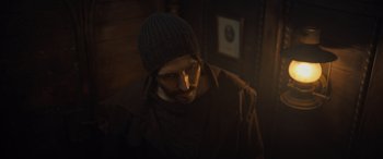 Movie still from “The Last Voyage of the Demeter” (2023), directed by André Øvredal – A man wearing a sweater and a hat is looking down; Close Up shot, High angle