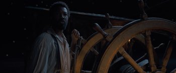 Movie still from “The Last Voyage of the Demeter” (2023), directed by André Øvredal – A man standing in front of a steering wheel; Medium shot, High angle