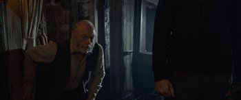 Movie still from “The Last Voyage of the Demeter” (2023), directed by André Øvredal – An old man with a beard is sitting in a dark room; Medium shot, Over the shoulder angle