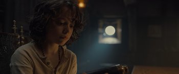 Movie still from “The Last Voyage of the Demeter” (2023), directed by André Øvredal – A young woman sitting in front of a television; Close Up shot, Low angle