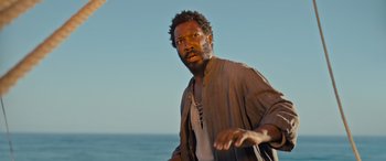 Movie still from “The Last Voyage of the Demeter” (2023), directed by André Øvredal – A man with a beard and a necklace is standing near the ocean; Close Up shot, Low angle