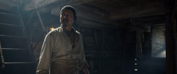 Movie still from “The Last Voyage of the Demeter” (2023), directed by André Øvredal – An old man standing in front of a log cabin; Medium shot, Low angle
