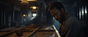 Movie still from “The Last Voyage of the Demeter” (2023), directed by André Øvredal – A man sitting at a table looking down at his head; Close Up shot, Low angle