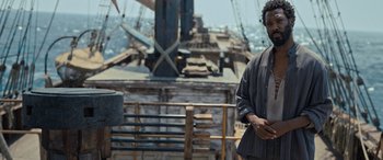 Movie still from “The Last Voyage of the Demeter” (2023), directed by André Øvredal – A man standing in front of an old boat; Medium shot, Over the shoulder angle