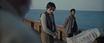 Movie still from “The Last Voyage of the Demeter” (2023), directed by André Øvredal – A man standing on a boat with another man standing next to him; Medium shot, Over the shoulder angle