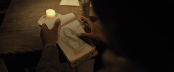 Movie still from “The Last Voyage of the Demeter” (2023), directed by André Øvredal – A person is drawing a picture in a book; Extreme Close Up shot, Over the shoulder angle