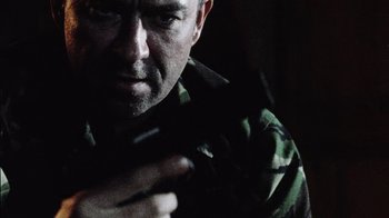 Movie still from “Dog Soldiers” (2002), directed by Neil Marshall – A man holding a gun while wearing a camouflage shirt; Close Up shot, Low angle