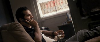 Movie still from “The Lincoln Lawyer” (2011), directed by Brad Furman – A man sitting on a couch holding a glass of alcohol; Medium shot, Over the shoulder angle