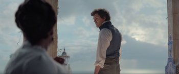 Movie still from “The Little Mermaid” (2023), directed by Rob Marshall – A man standing next to a wall looking at something; Medium shot, Over the shoulder angle