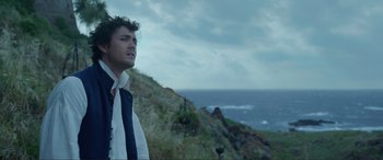 Movie still from “The Little Mermaid” (2023), directed by Rob Marshall – A man standing on top of a hill near the ocean; Medium shot, Low angle