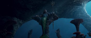 Movie still from “The Little Mermaid” (2023), directed by Rob Marshall – A woman is standing in the water holding a trident; Wide shot, High angle