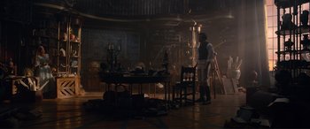 Movie still from “The Little Mermaid” (2023), directed by Rob Marshall – A man standing next to a table in a dimly - lit room; Wide shot, Low angle