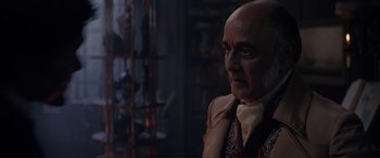 Movie still from “The Little Mermaid” (2023), directed by Rob Marshall – An older man with a bald head wearing a tie; Close Up shot, Over the shoulder angle