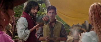 Movie still from “The Little Mermaid” (2023), directed by Rob Marshall – Two men standing next to each other holding a pair of shoes; Medium shot, Low angle