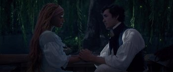 Movie still from “The Little Mermaid” (2023), directed by Rob Marshall – A man and a woman holding hands in front of a tree; Medium shot, High angle