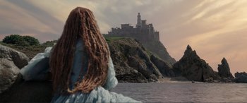 Movie still from “The Little Mermaid” (2023), directed by Rob Marshall – A woman in a dress looking at a castle on a hill; Extreme Wide shot, Low angle