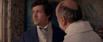 Movie still from “The Little Mermaid” (2023), directed by Rob Marshall – A man wearing a suit and tie next to a man with a bald head; Close Up shot, Over the shoulder angle