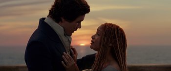 Movie still from “The Little Mermaid” (2023), directed by Rob Marshall – A man and a woman standing next to each other in front of a sunset; Medium shot, High angle