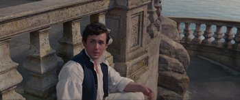 Movie still from “The Little Mermaid” (2023), directed by Rob Marshall – A young man sitting on the ground in front of a stone wall; Medium shot, High angle