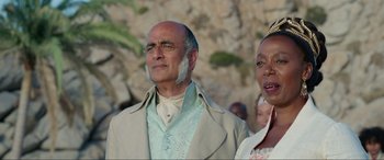 Movie still from “The Little Mermaid” (2023), directed by Rob Marshall – An older man and a woman standing next to each other in front of a rock wall; Close Up shot, Low angle