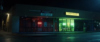 Movie still from “The Locksmith” (2023), directed by Nicolas Harvard – A night time photo of a store front with neon lights; Extreme Wide shot, Low angle