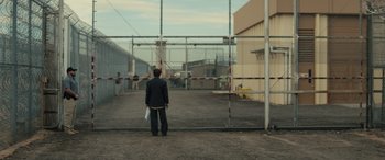 Movie still from “The Locksmith” (2023), directed by Nicolas Harvard – A man standing in front of a gate; Extreme Wide shot, Over the shoulder angle