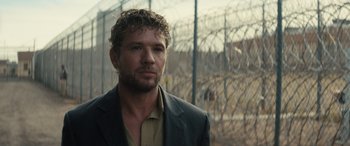 Movie still from “The Locksmith” (2023), directed by Nicolas Harvard – A person wearing a suit near a fence; Close Up shot, Over the shoulder angle