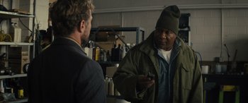 Movie still from “The Locksmith” (2023), directed by Nicolas Harvard – A man in a green jacket talking to another man in a black suit; Medium shot, Over the shoulder angle