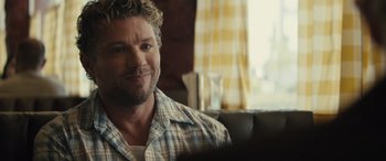 Movie still from “The Locksmith” (2023), directed by Nicolas Harvard – A person sitting on a couch near a window; Close Up shot, Over the shoulder angle