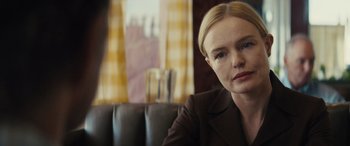 Movie still from “The Locksmith” (2023), directed by Nicolas Harvard – A person sitting on a couch in a room; Close Up shot, Over the shoulder angle