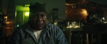 Movie still from “The Locksmith” (2023), directed by Nicolas Harvard – A person wearing a jacket and a hat; Close Up shot, Low angle