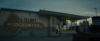Movie still from “The Locksmith” (2023), directed by Nicolas Harvard – An old building with a sign on the side of the building; Extreme Wide shot, High angle