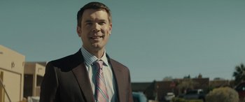 Movie still from “The Locksmith” (2023), directed by Nicolas Harvard – A man in a suit and tie smiling for the camera; Close Up shot, Over the shoulder angle