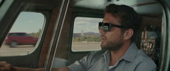 Movie still from “The Locksmith” (2023), directed by Nicolas Harvard – A man driving in a car with sunglasses on; Close Up shot, Low angle