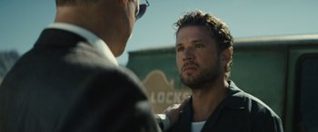 Movie still from “The Locksmith” (2023), directed by Nicolas Harvard – A man standing next to another man in a parking lot; Close Up shot, Over the shoulder angle